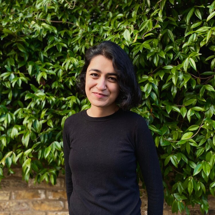 This is a photo of a woman in front of a leafy background.