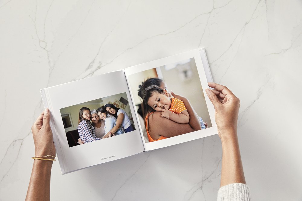 A woman's hands holding a photo album showing a group shot and a woman with a baby in her arms.