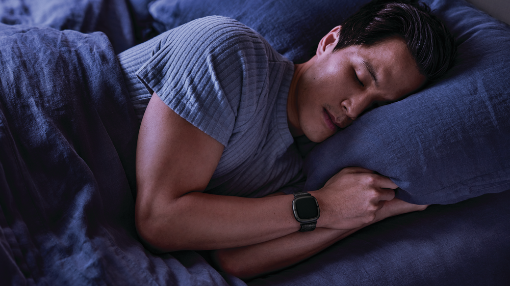 A man sleeps with Sense 2 on his wrist, tracking his sleep patterns for advanced insights.